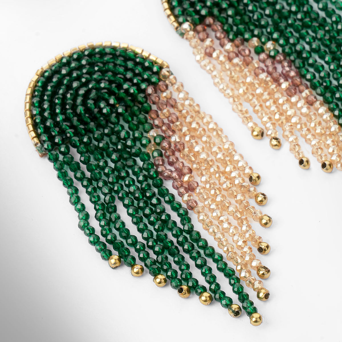 A close-up of beaded fringe earrings on a white background, featuring multiple strands of beads in dark green and champagne, accented with small gold beads.