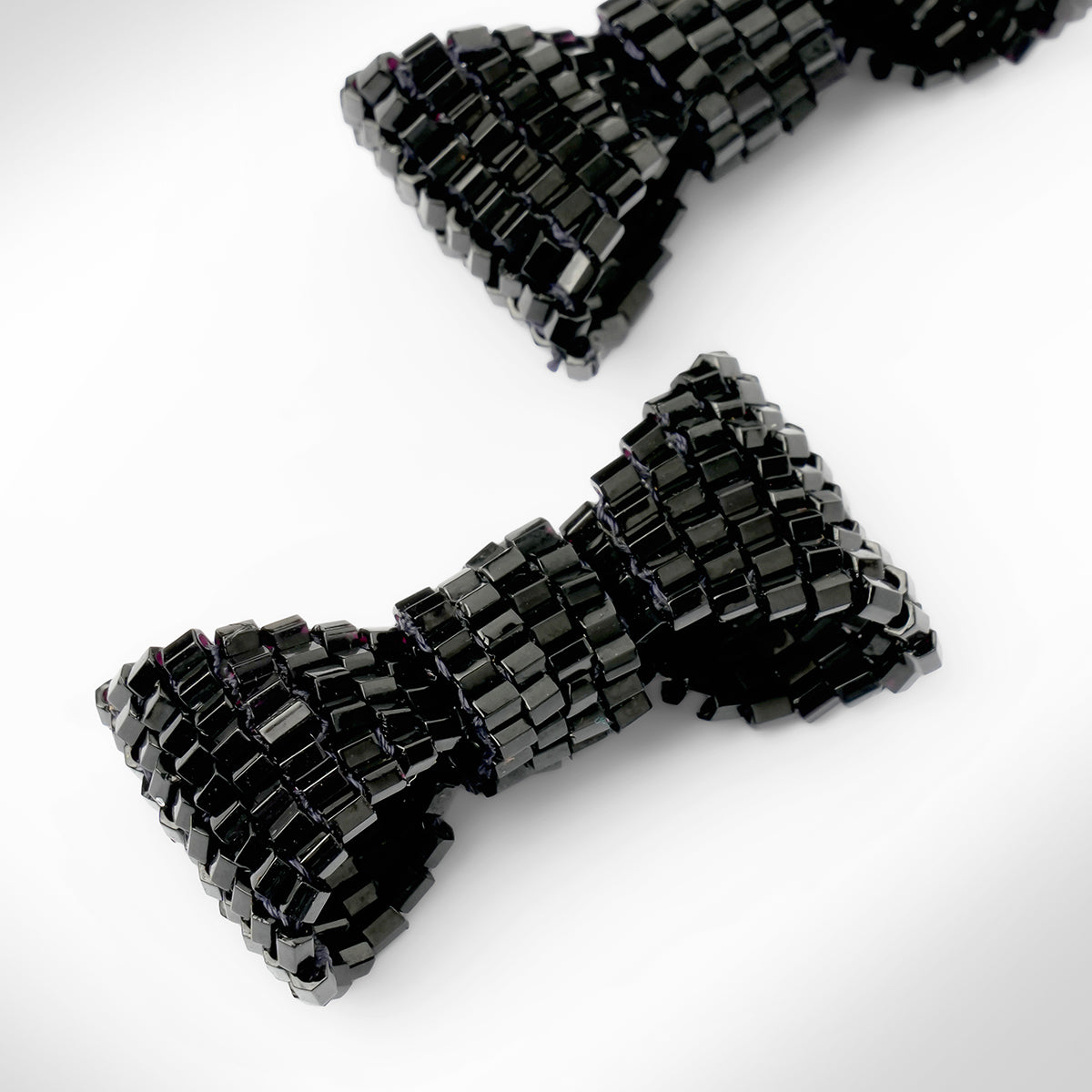 Close up of black beaded bow-shaped earrings on a light gray gradient background.