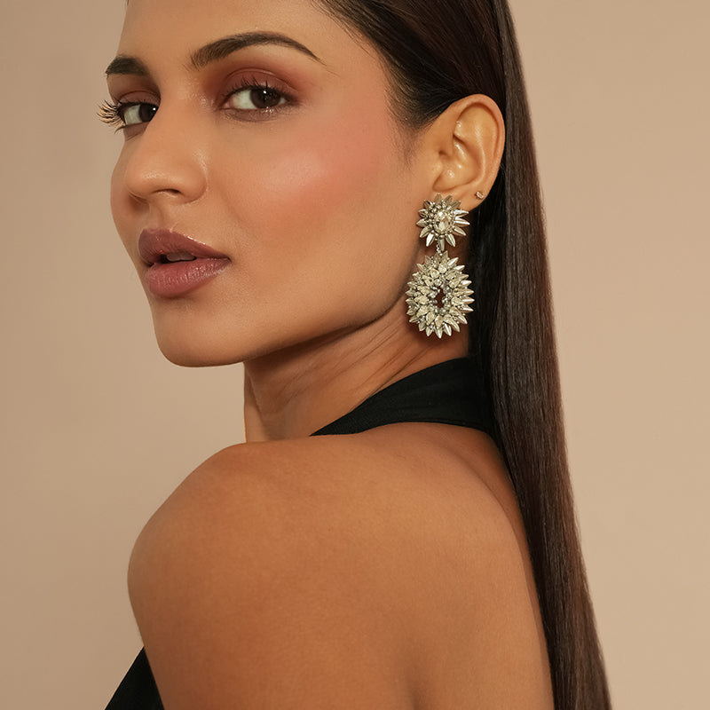 Woman wearing a pair of large, ornate earrings against a beige background
