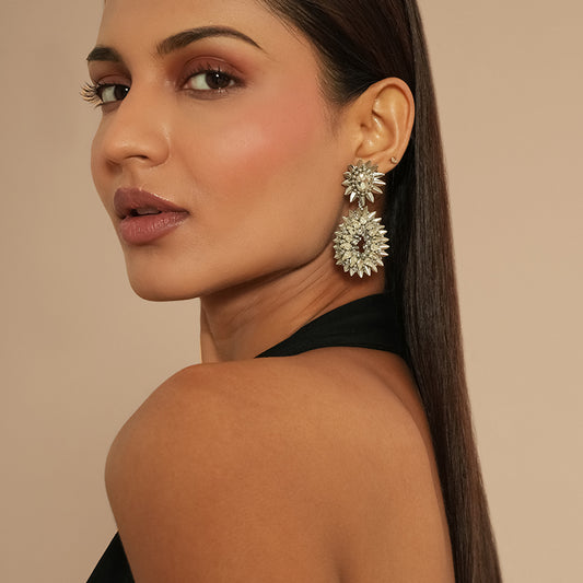 Woman wearing a pair of large, ornate earrings against a beige background