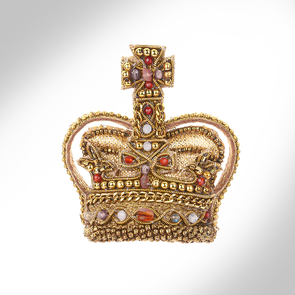 An ornate gold tone crown brooch decorated with red, white, and purple stones, set against a light gray gradient background.