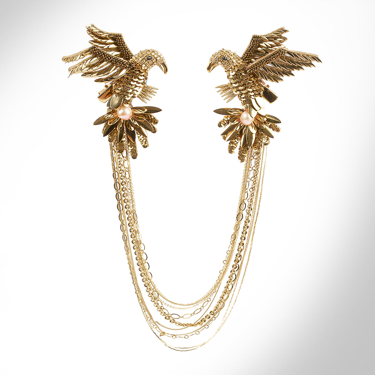 A gold-toned brooch featuring detailed bird motifs with multiple dangling chain layers, displayed on a grey background.