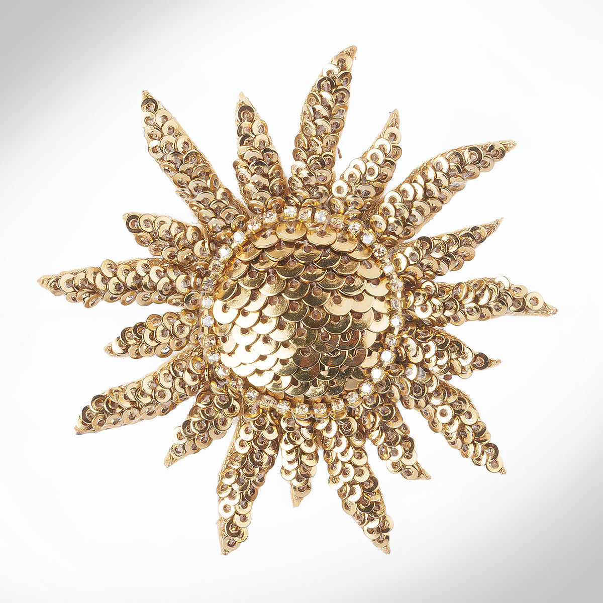 A gold sunburst brooch embellished with sequins and shown on a light gray gradient background.