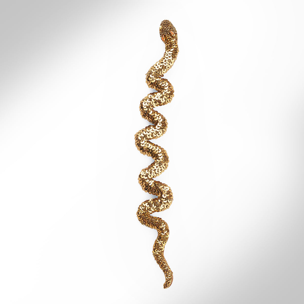 A gold tone snake brooch embellished with sequins shown against a light gray gradient background.
