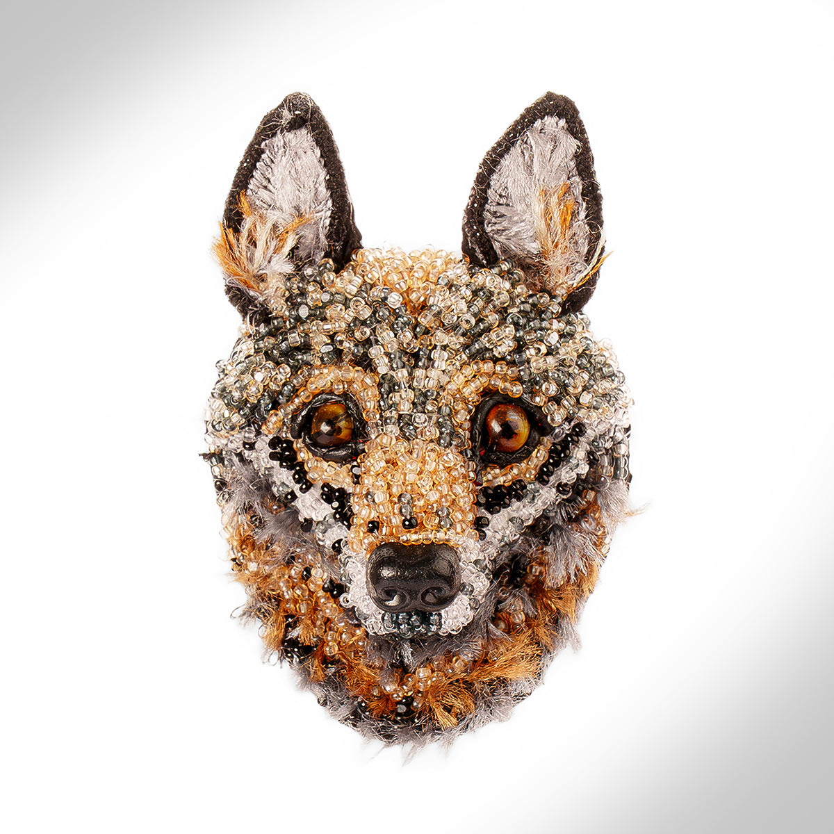 A detailed beaded wolf brooch, featuring intricate beadwork in shades of brown, black, white, and orange, with fur-like textures around the muzzle and ears, set against a clean white background.