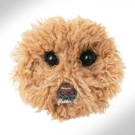 A round, fluffy tan dog brooch shown on a white background.