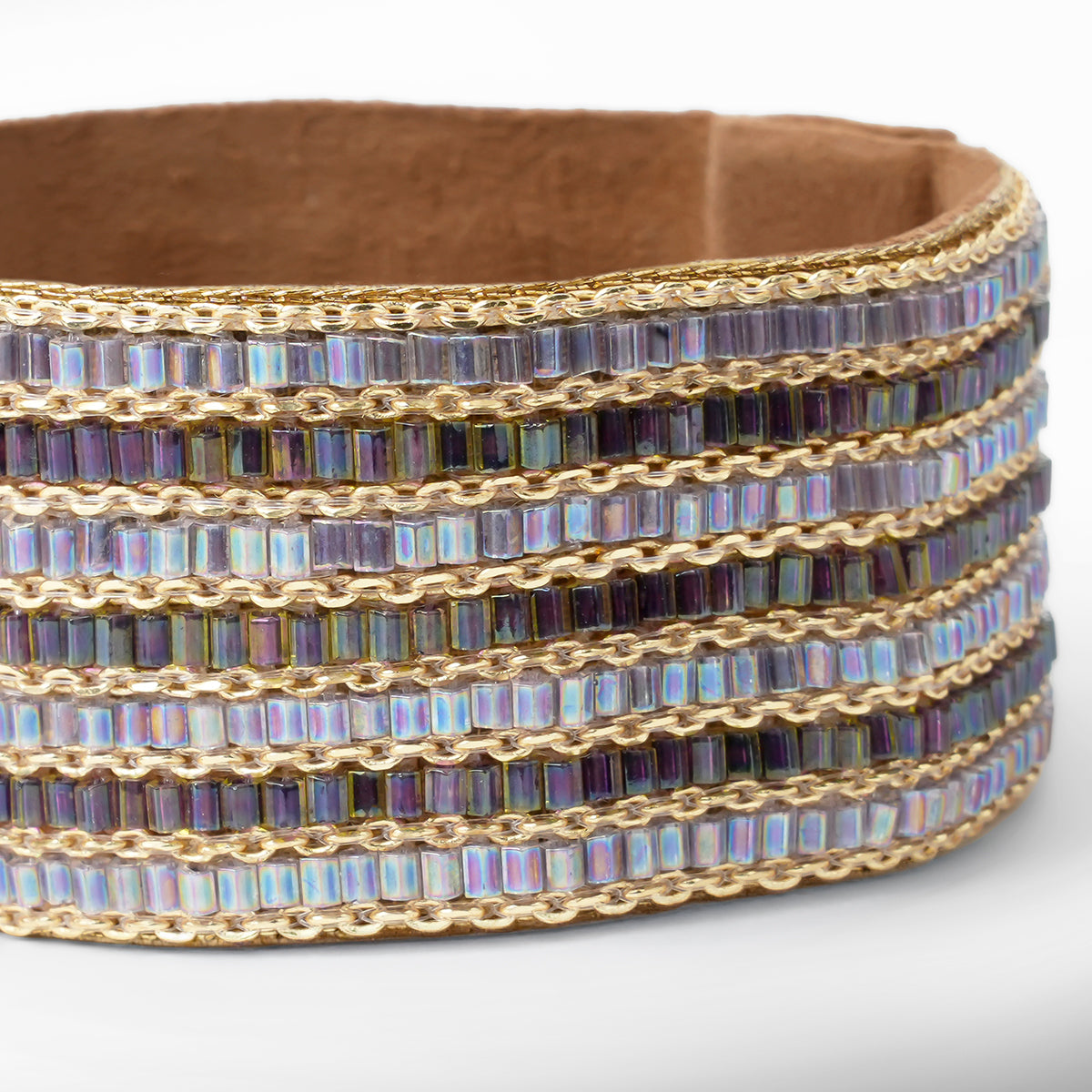 A wide beaded cuff bracelet featuring and iridescent beads, gold chain links,  set against a neutral gray background.