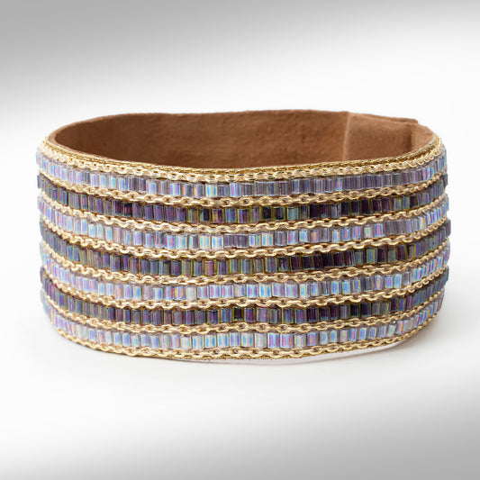 A wide, multi-row beaded cuff bracelet with iridescent rectangular beads in shades of purple, blue, and gold, set against a neutral gray background.