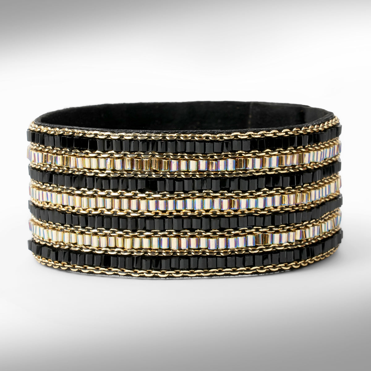 A wide beaded cuff bracelet featuring black faceted beads, gold chain links, and iridescent beads set against a neutral gray background.
