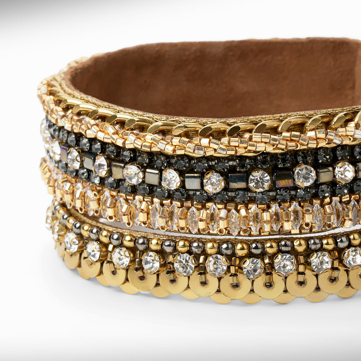 Close up of a gold-tone bracelet with mixed crystal and bead embellishments, shown on a light gray gradient background.