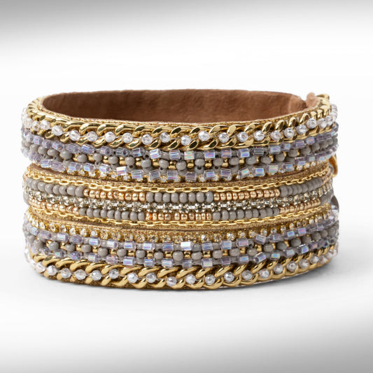 A gold-tone bracelet with mixed textures including chain links, beads, and clear stones, set against a light gray background.