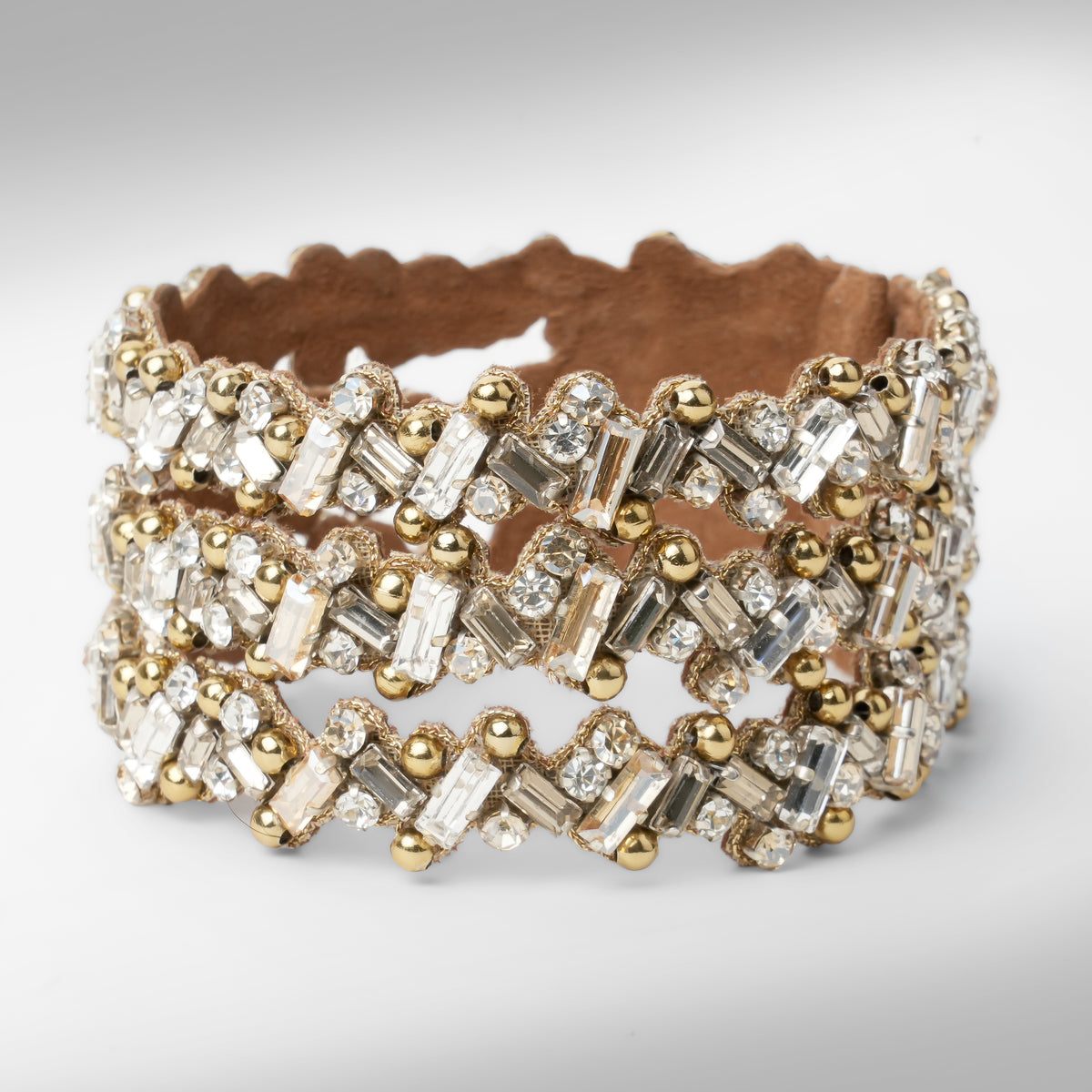 A wide gold-tone cuff bracelet embellished with multiple rows of champagne and silver-toned rectangular and round crystals, set against a plain white background.