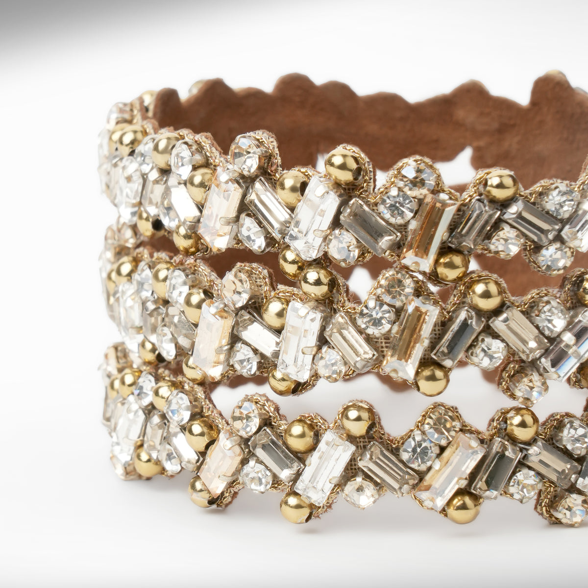 A close-up of a wide gold-tone cuff bracelet embellished with multiple rows of champagne and silver-toned rectangular and round crystals, set against a plain white background.