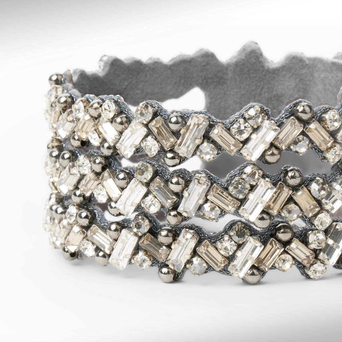 a wide silver-tone cuff bracelet embellished with multiple rows of gunmetal and silver-toned rectangular and round crystals, set against a plain white background.