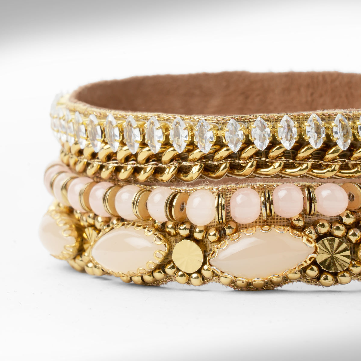 A close-up of a gold-toned beaded and rhinestone bracelet with pale pink beads and oval stone accents, photographed on a clean white background.