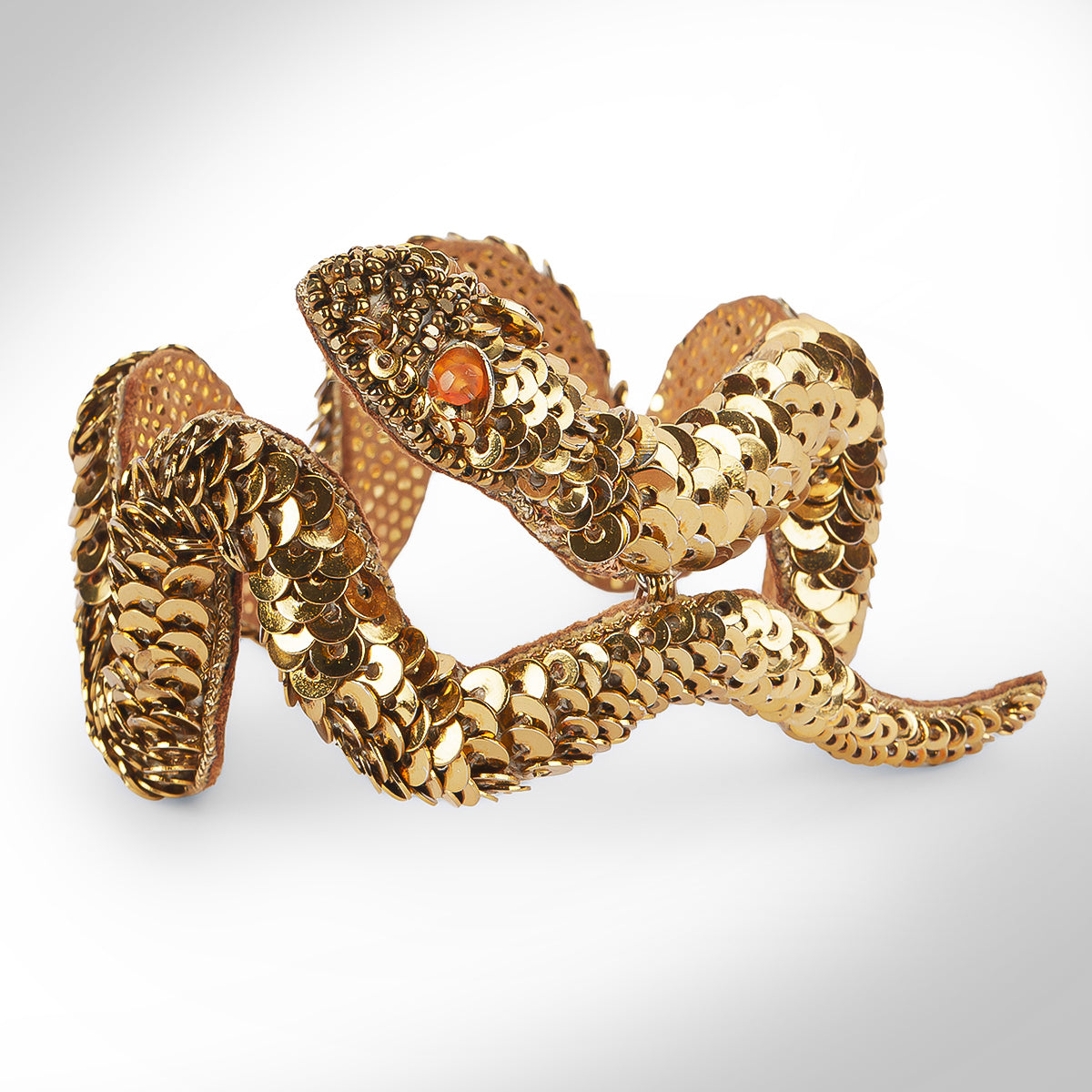 A gold tone snake-shaped cuff bracelet embellished with sequins photographed on a light gray gradient background.