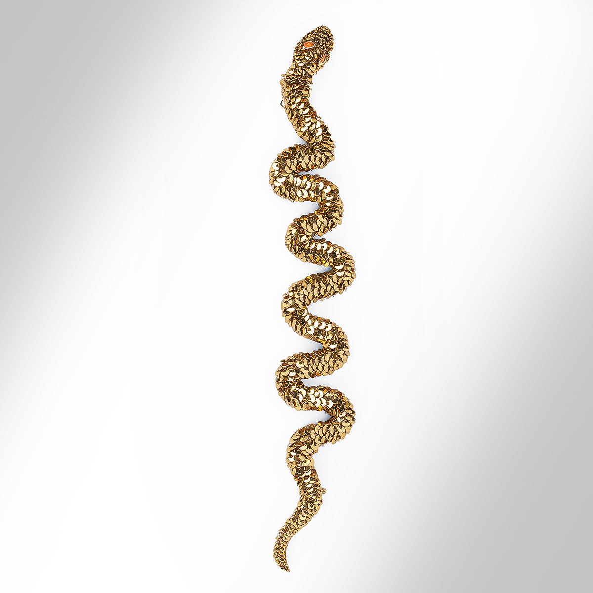 A gold tone snake-shaped cuff bracelet embellished with sequins photographed on a light gray gradient background.