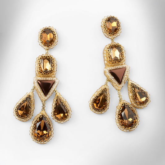 A pair of ornate gold-toned statement earrings with faceted brown and amber gemstones, displayed on a clean light gray background.