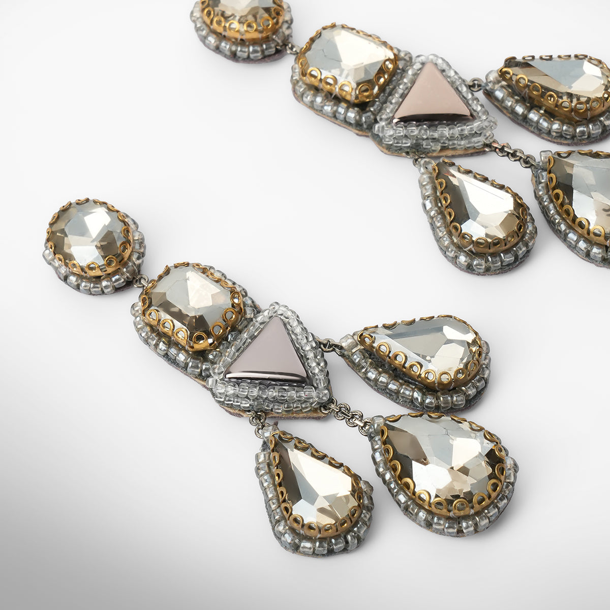 Close up of a pair of ornate silver-toned statement earrings with faceted gunmetal and silver stones, displayed on a clean light gray background.