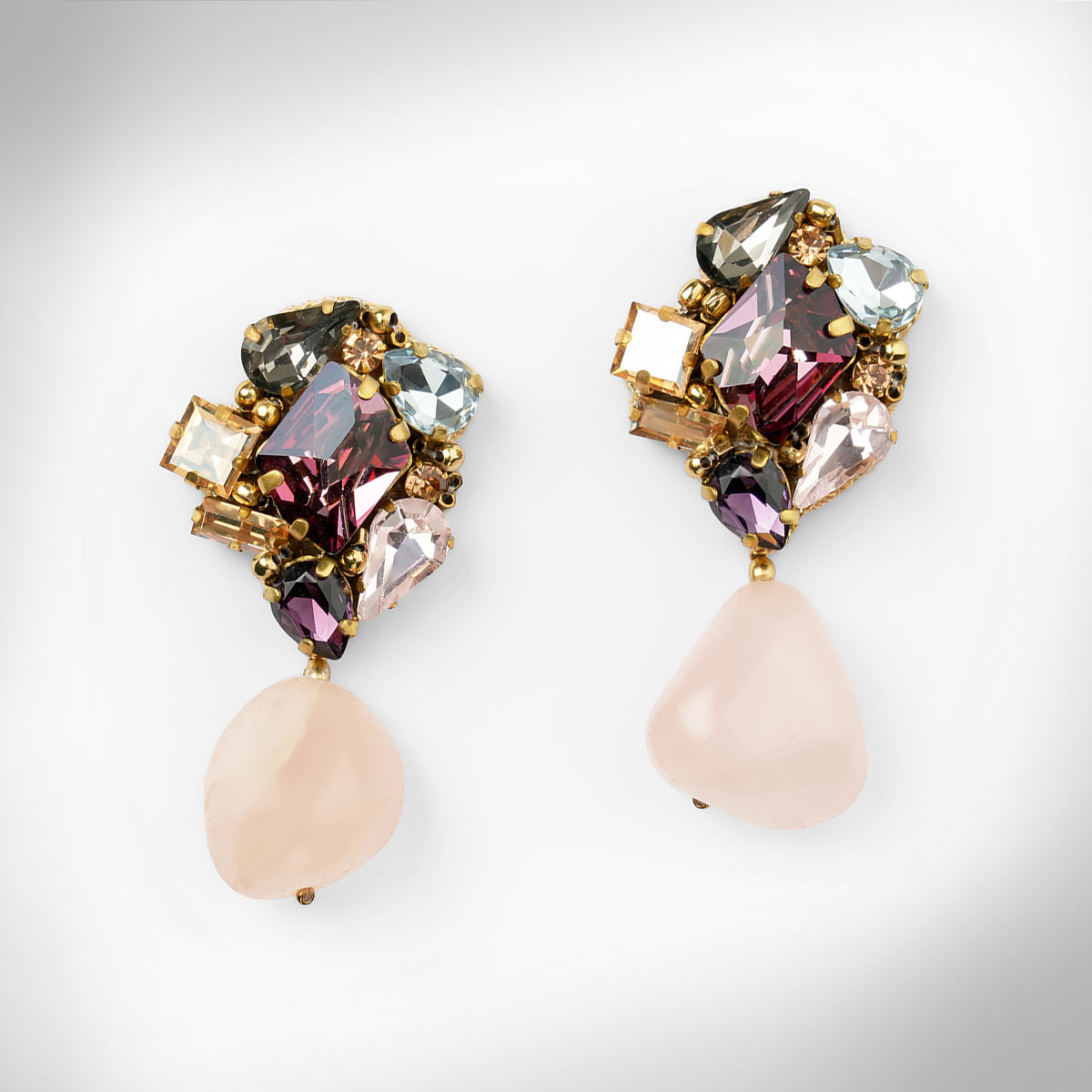 A pair of gold-tone drop earrings featuring a cluster of multicolored faceted crystals at the top and a teardrop-shaped pale pink stone dangling below each earring, shown on a light gray background.