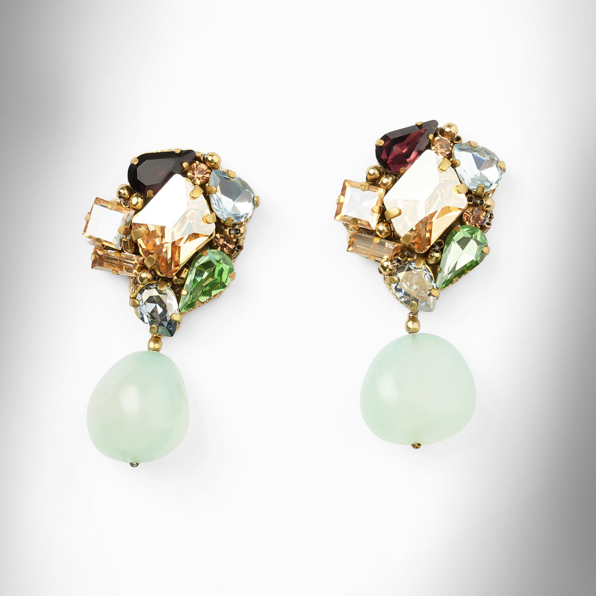 A pair of gold-tone drop earrings featuring a cluster of multicolored faceted crystals at the top and a teardrop-shaped mint stone dangling below each earring, shown on a light gray background.