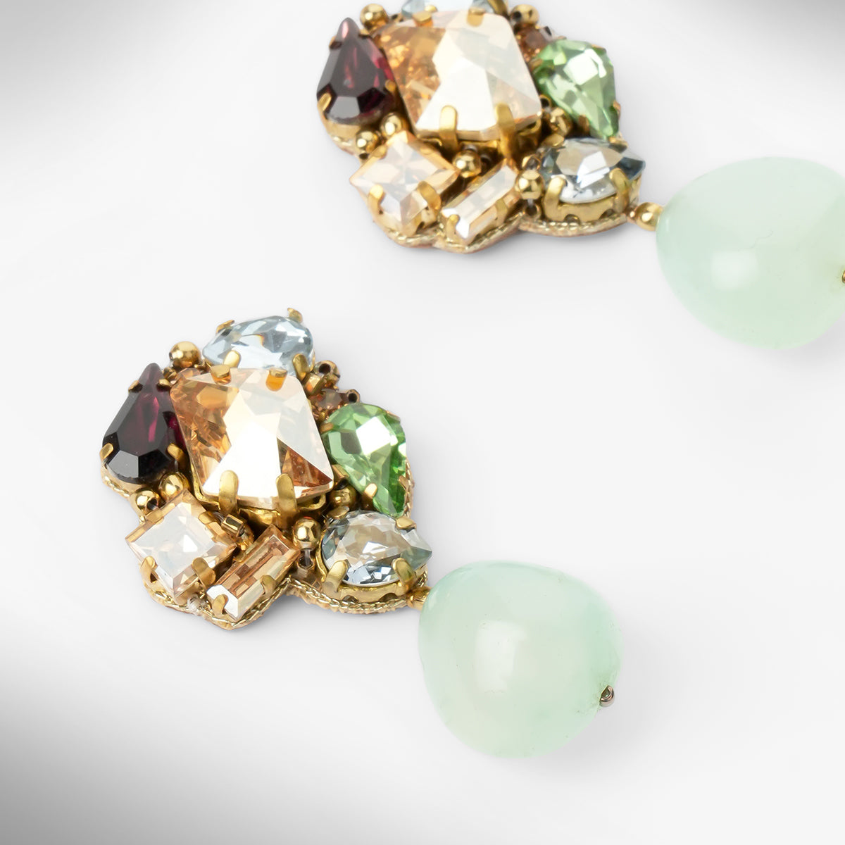 Close up of a pair of gold-tone drop earrings featuring a cluster of multicolored faceted crystals at the top and a teardrop-shaped mint stone dangling below each earring, shown on a light gray background.