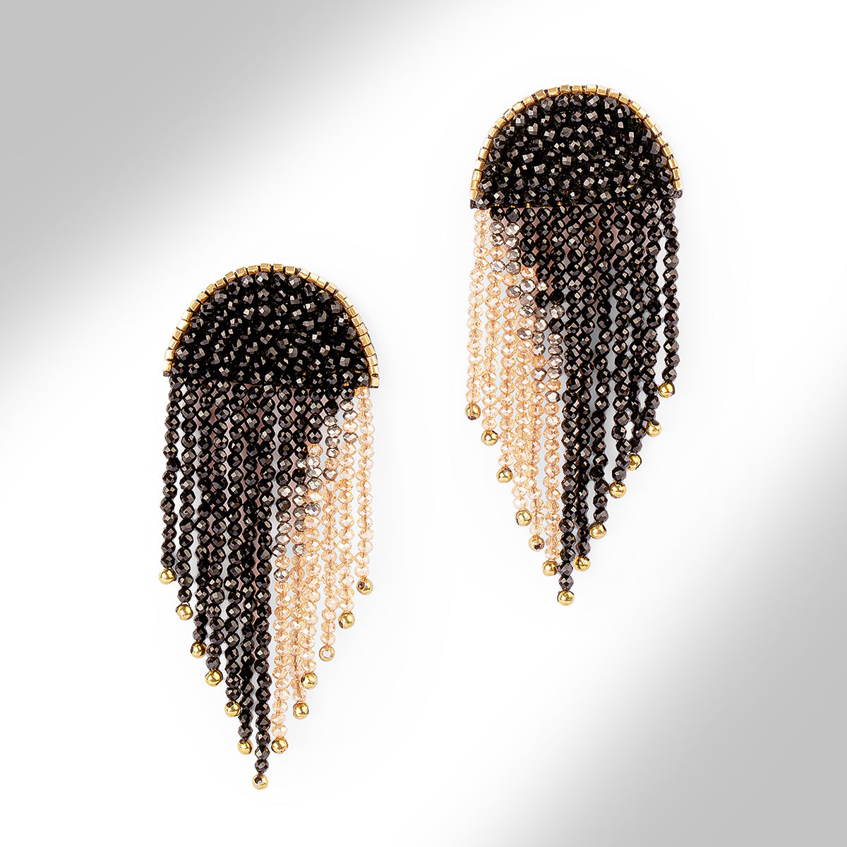 A pair of beaded fringe earrings with a black top section, transitioning into pale champagne beads, finished with small gold beads at the tips, shown on a light gray gradient background.