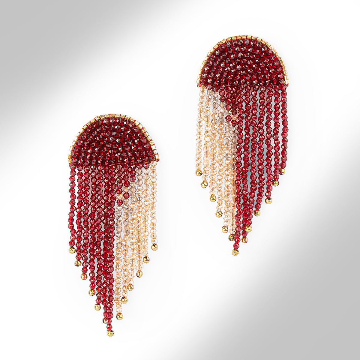 A pair of beaded fringe earrings with a dark red top section, transitioning into pale champagne beads, finished with small gold beads at the tips, shown on a light gray gradient background.