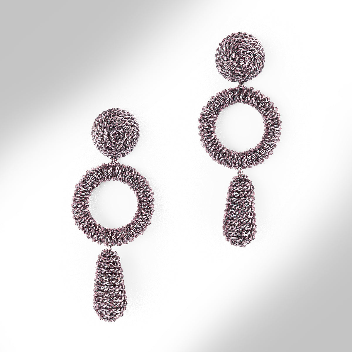 A pair of textured, multi-layered dangle earrings in a metallic finish on a light gray gradient background.