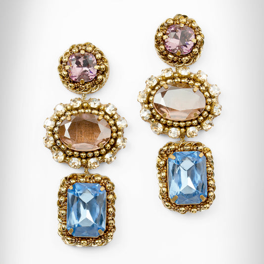 A pair of ornate gold-tone drop earrings with pink, peach, and light blue faceted stones surrounded by champagne stones, shown on a light gray background.