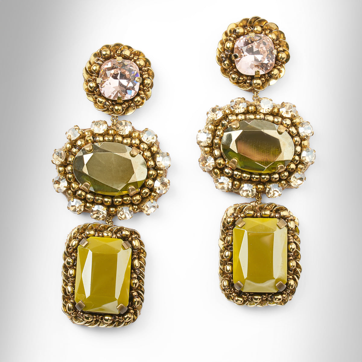 A pair of ornate gold-tone drop earrings with pink, green, and olive faceted stones surrounded by champagne stones, shown on a light gray background.