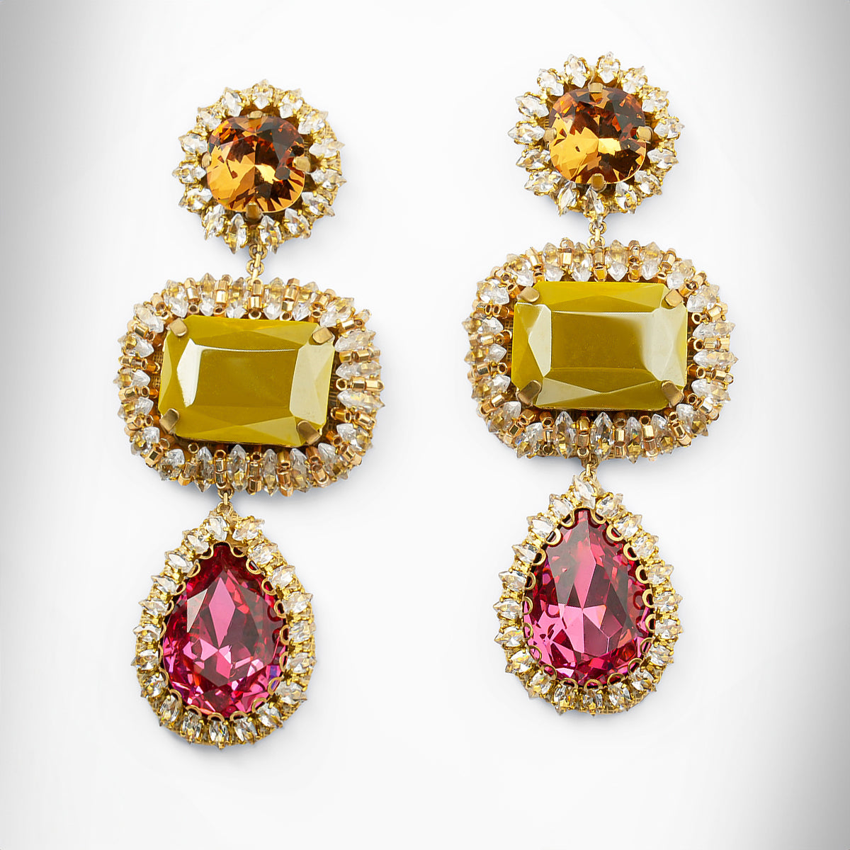 A pair of ornate drop earrings with olive and pink stones surrounded by clear stones on a light gray background.