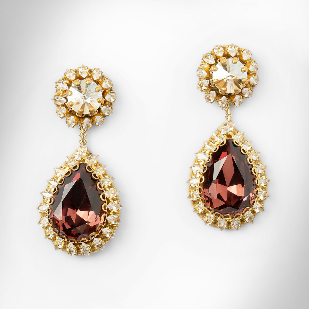 A pair of gold tone drop earrings featuring a champagne top and a larger teardrop-shaped brown stone below, surrounded by small clear stones.