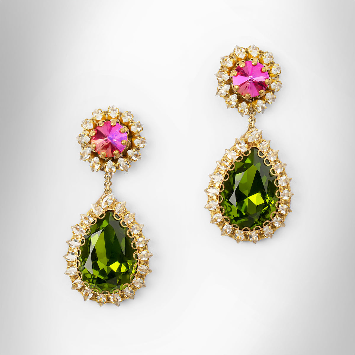 A pair of gold tone drop earrings featuring a fuchsia top and a larger teardrop-shaped green stone below, surrounded by small clear stones.