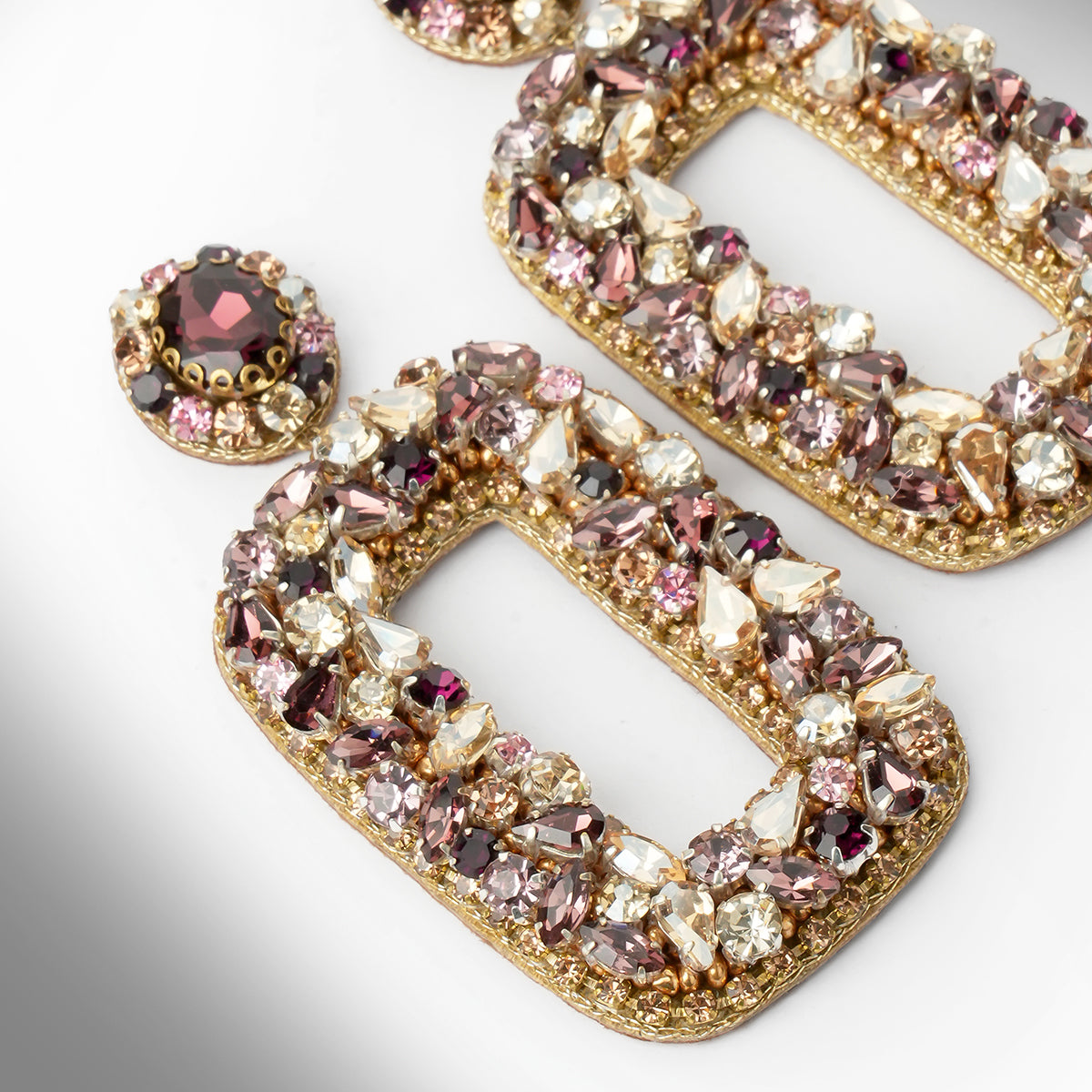 Gold-tone statement earrings adorned with an array of pink, amethyst, champagne, and clear faceted crystals, shown in a close-up studio shot on a white background.