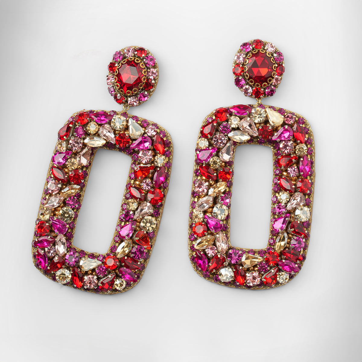 A pair of statement drop earrings featuring large open rectangular shapes densely embellished with pink, red, and gold-toned stones shown on a light gray background.