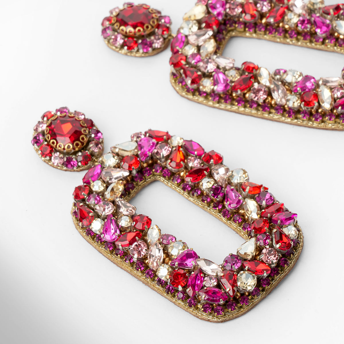 Gold-tone statement earrings adorned with vibrant pink, red, and clear stones, shown in a close-up studio shot on a white background.