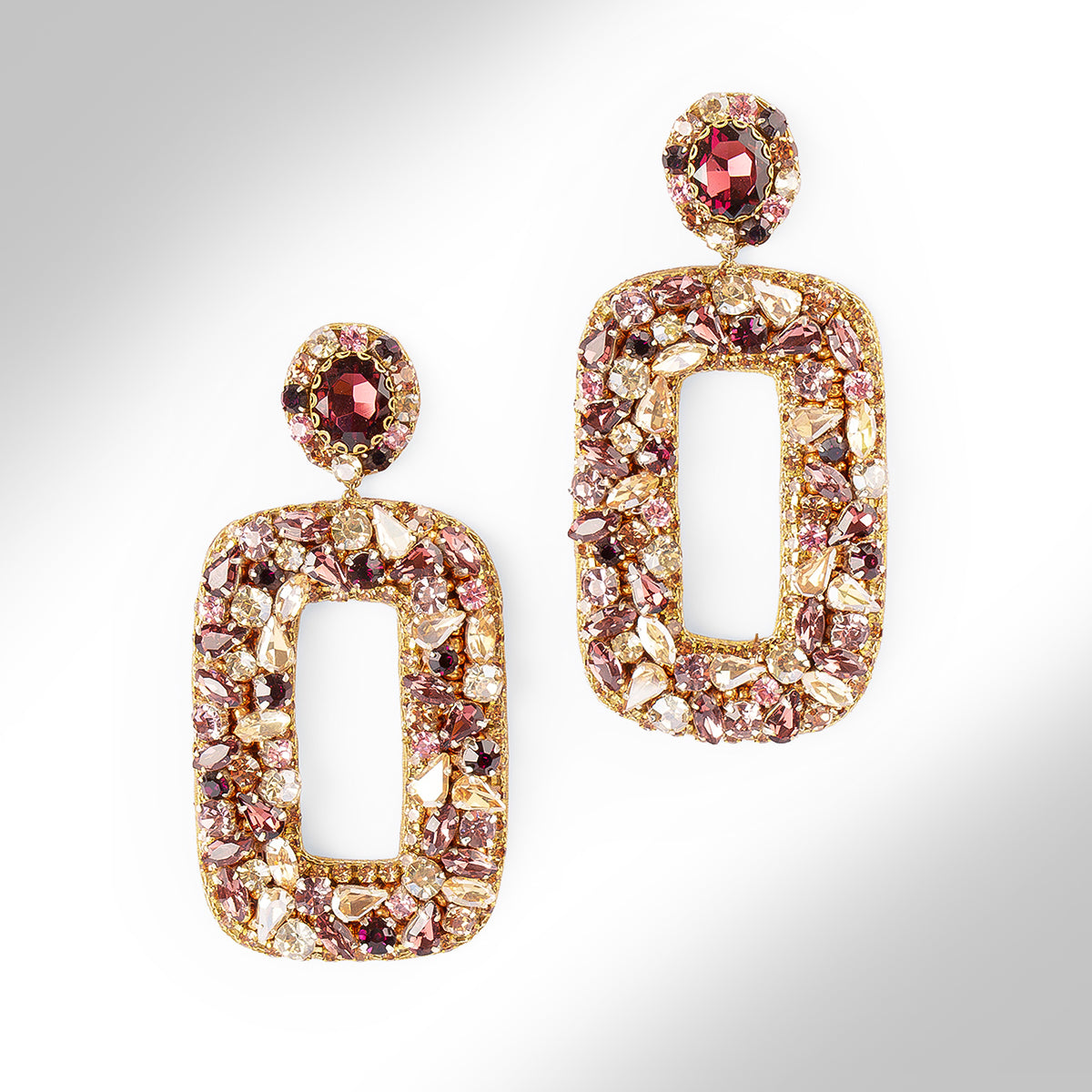 Gold-tone statement earrings adorned with an array of pink, amethyst, champagne, and clear faceted crystals, shown in a close-up studio shot on a white background.