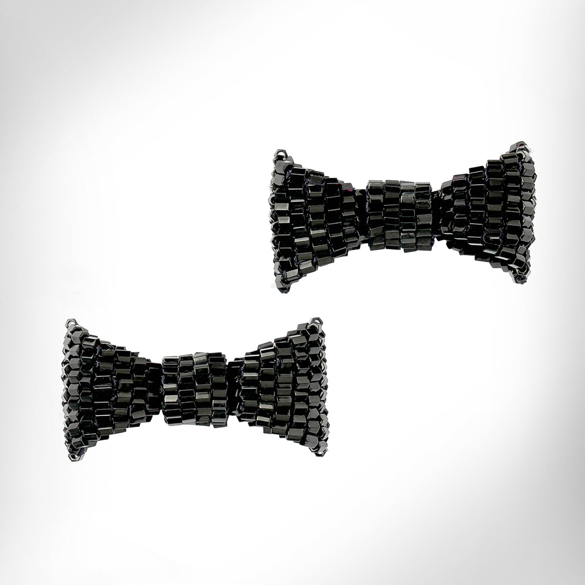 Black beaded bow-shaped earrings on a light gray gradient background.