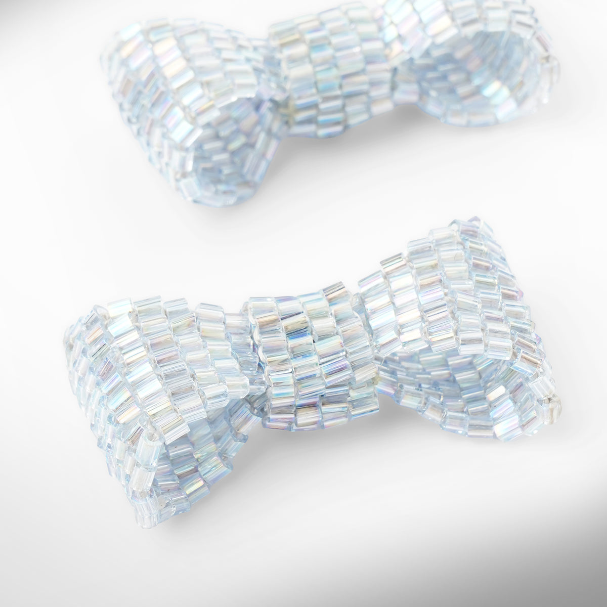 Close up of baby blue beaded bow-shaped earrings on a light gray gradient background.