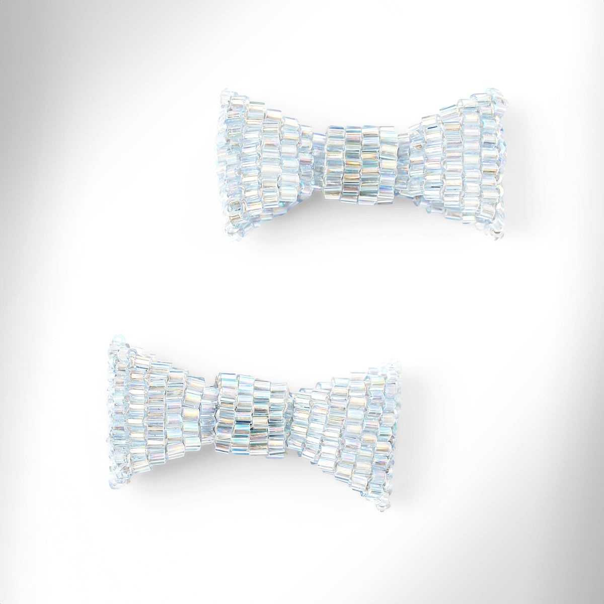 Baby blue beaded bow-shaped earrings on a light gray gradient background.