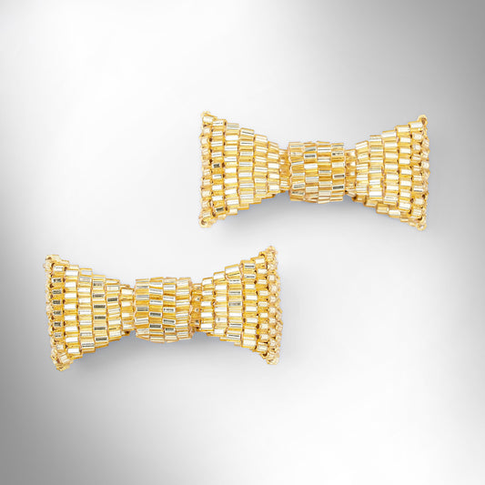 Gold beaded bow-shaped earrings on a light gray gradient background.