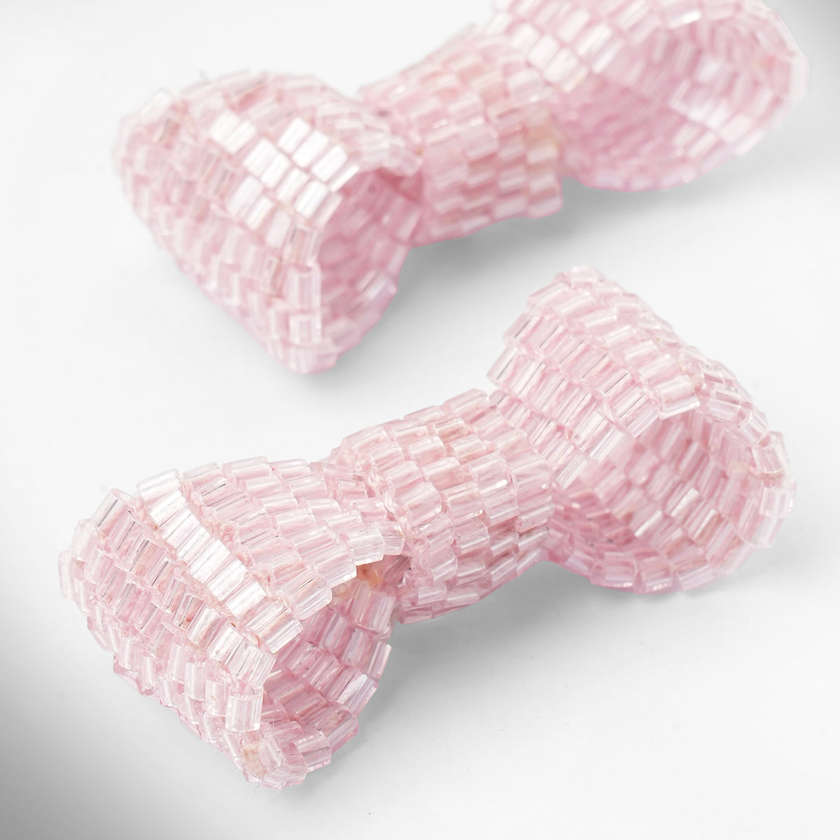 Close up of baby pink beaded bow-shaped earrings on a light gray gradient background.