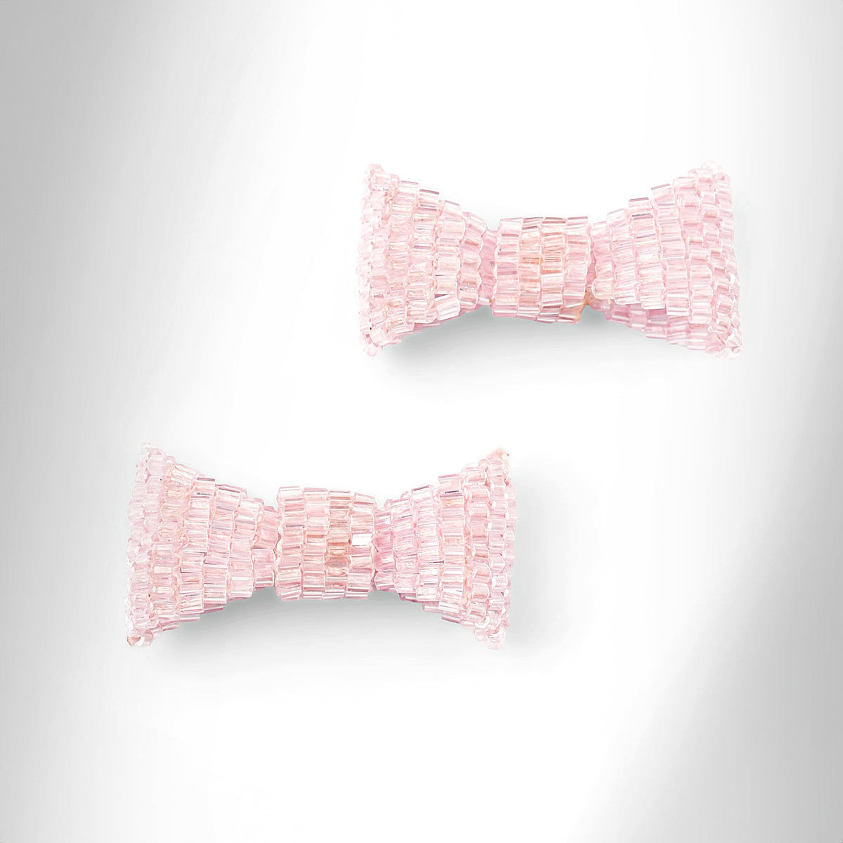 Baby pink beaded bow-shaped earrings on a light gray gradient background.