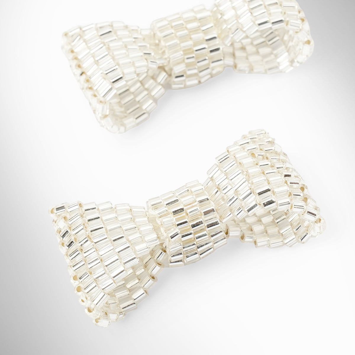 Close up of silver beaded bow-shaped earrings on a light gray gradient background.