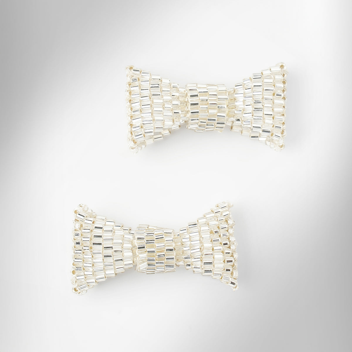 Silver beaded bow-shaped earrings on a light gray gradient background.