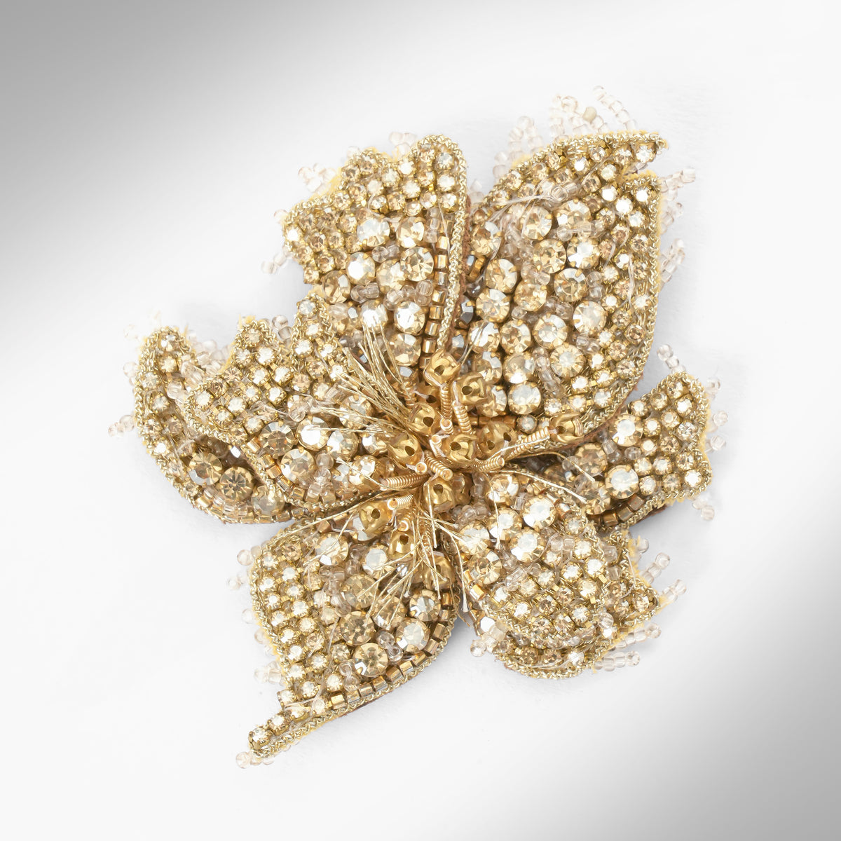 Close up of a pair of floral earrings adorned with gold stones and set in gold-toned metal, displayed on a light gray background.