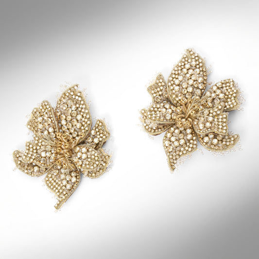 A pair of floral earrings adorned with gold stones and set in gold-toned metal, displayed on a light gray background.