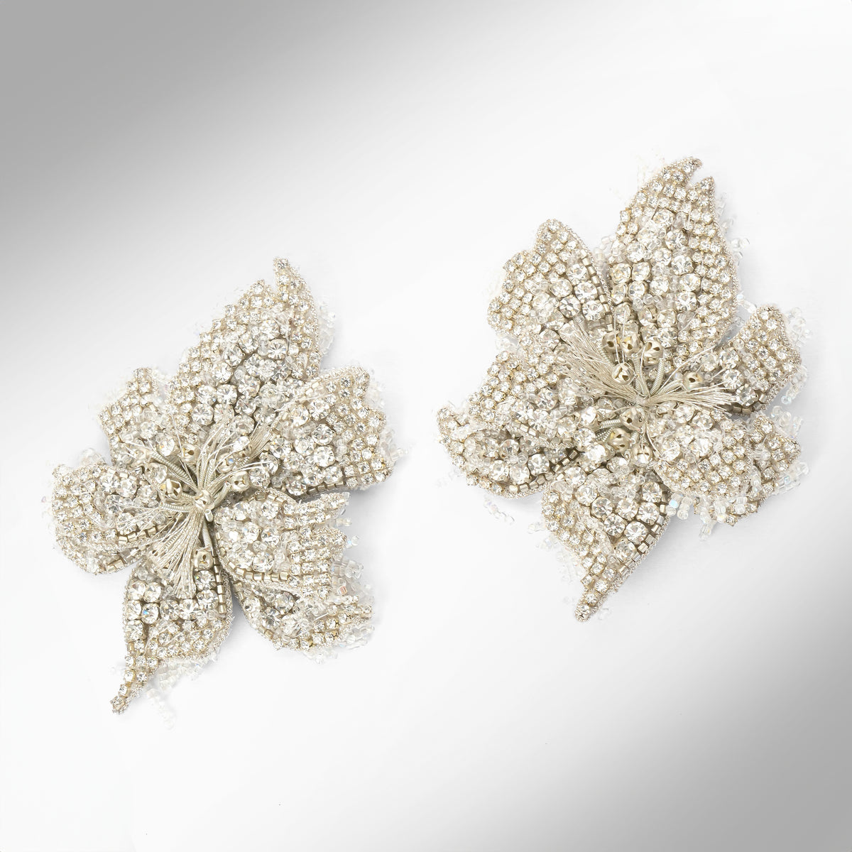 A pair of floral earrings adorned with silver stones and set in silver-toned metal, displayed on a light gray background.