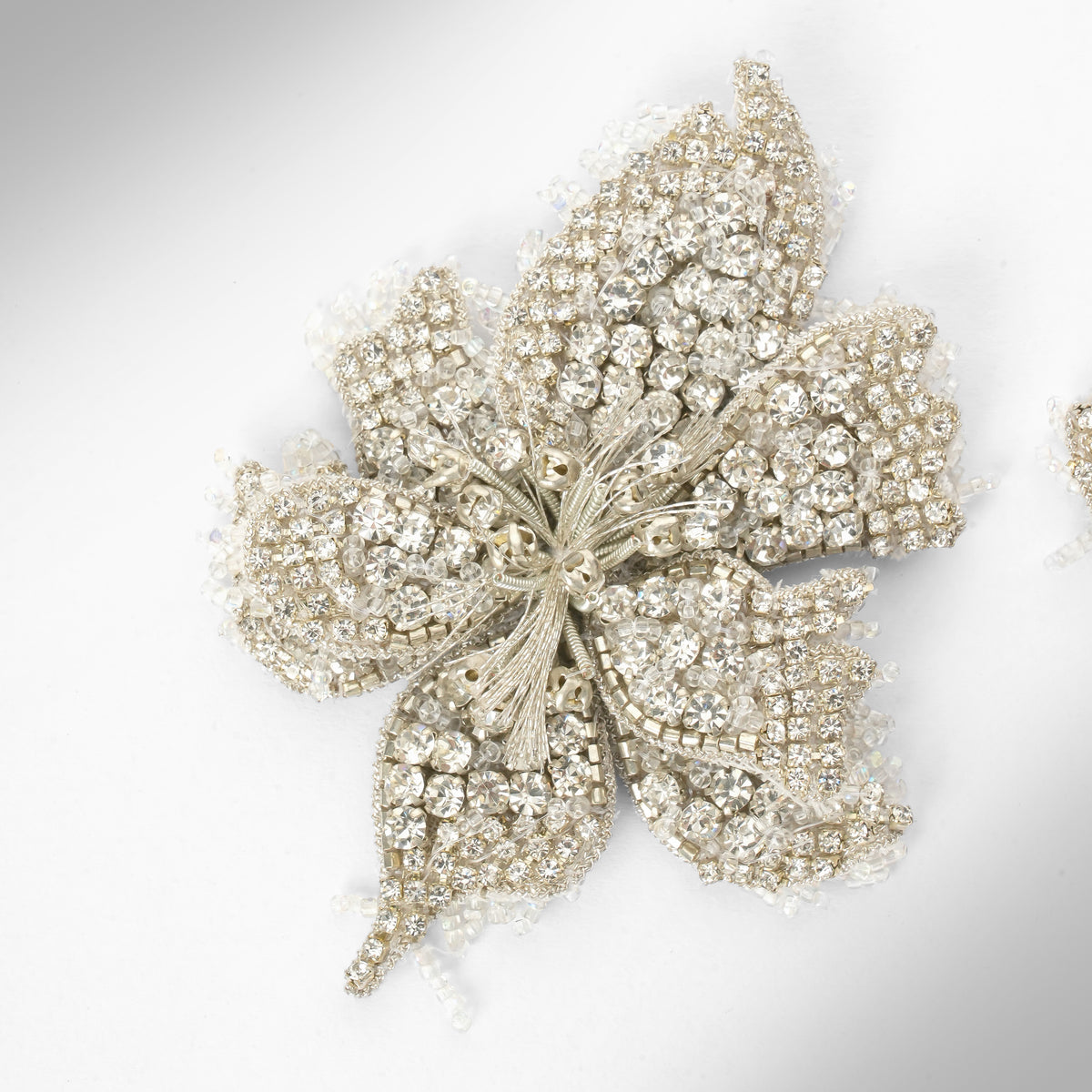 Close up of a pair of floral earrings adorned with silver stones and set in silver-toned metal, displayed on a light gray background.